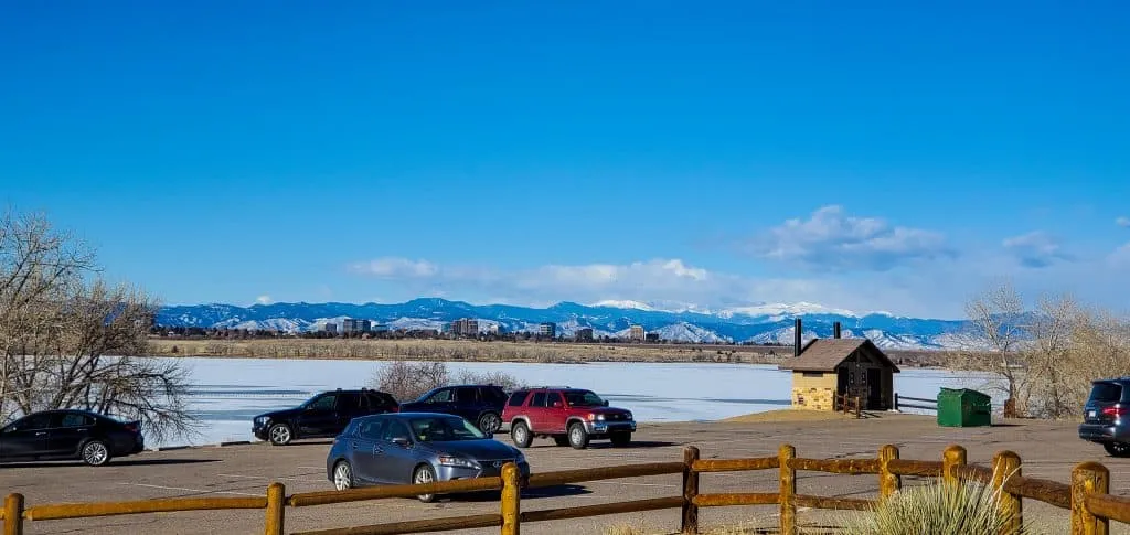 Parking lot with cars and restroom building at Cherry Creek State Park, Aurora, Colorado, frozen reservoir, Rocky Mountains in the distance