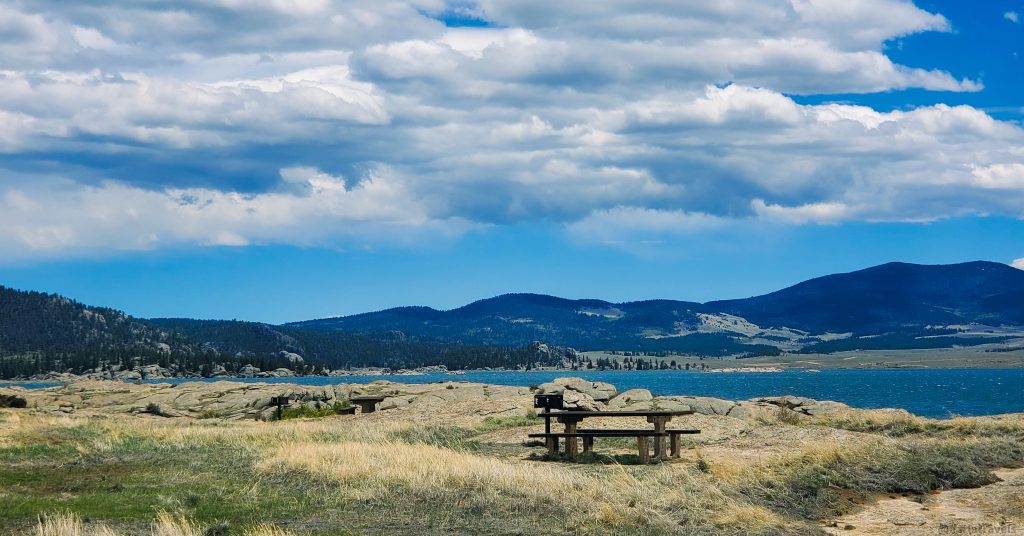 Eleven Mile Reservoir, mountains in the distance, day use picnic area with picnic table and grill in the foreground.  