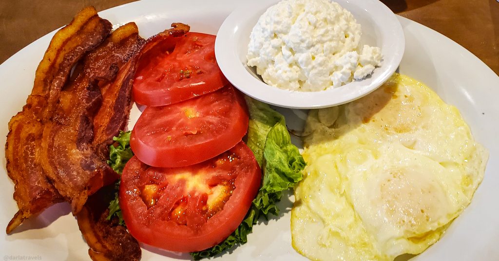 crispy bacon, tomato slices on lettuce, cottage cheese and fried eggs on a white oval plate