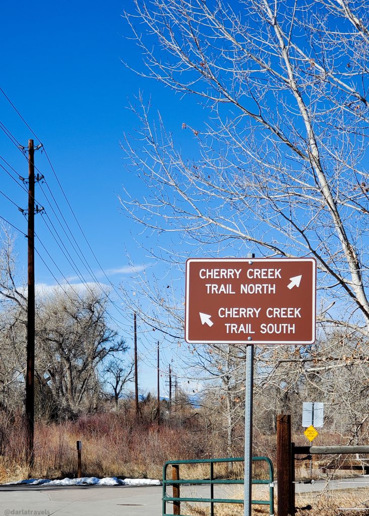 rectangular brown sign with white lettering pointing the way to the Cherry Creek Trail North and Cherry Creek Trail South 