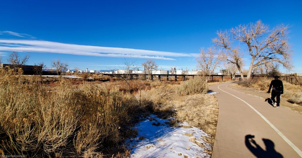 paved bike path, industrial area with large white cylindrical buildings in the distance. 