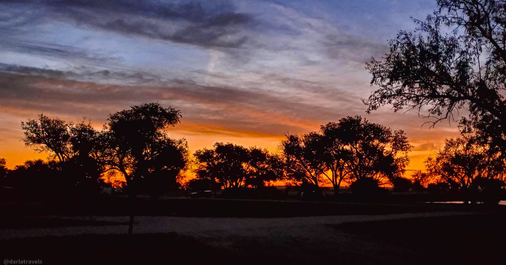 Silhouette of trees against a vibrant orange and purple sunrise sky in John Martin Reservoir State Park