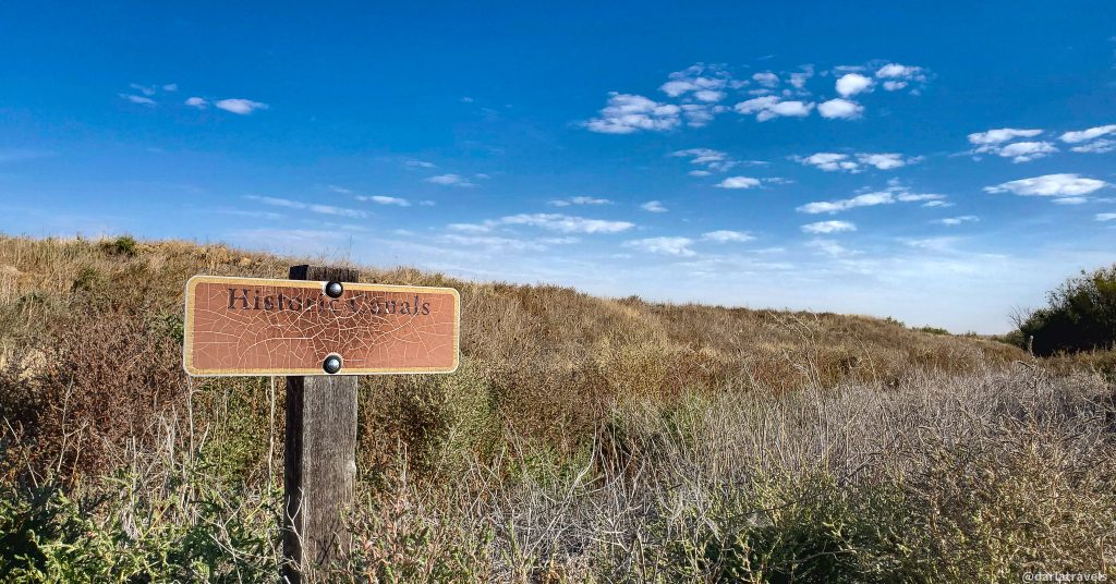 Historic canals signpost in a dry, grassy landscape under a clear blue sky.