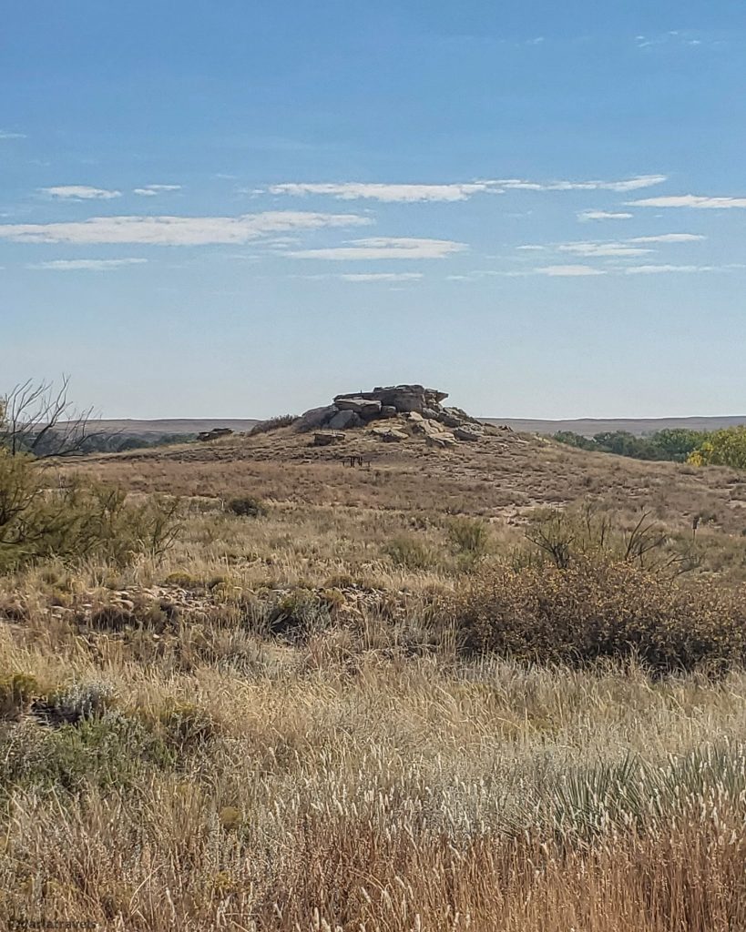 A rocky outcrop of Dakota sandstone sits atop a dry, grassy hill under a clear blue sky.