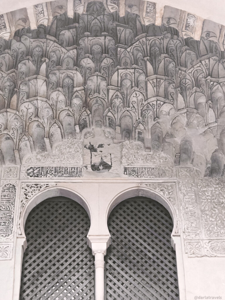 A close-up of an ornate Moorish archway. The arch is decorated with intricate stuccowork and features a geometric pattern.