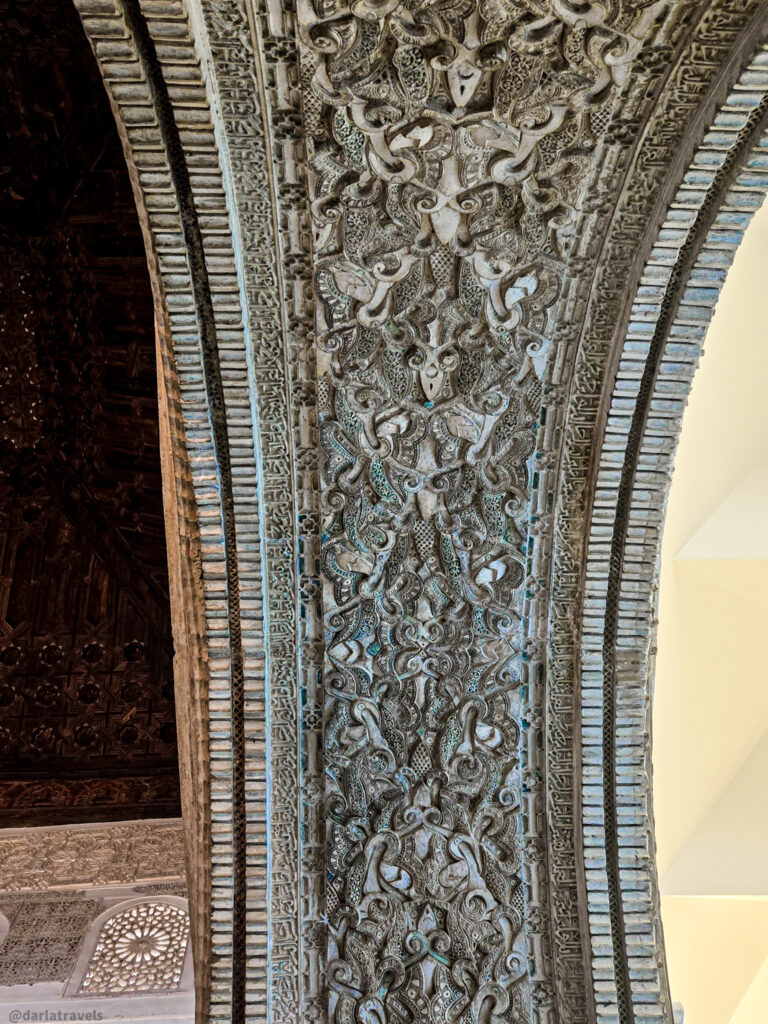 A close-up of an ornate stucco ceiling with a complex pattern of stylized leaves, flowers, and arabesques. The stuccowork creates a sense of depth and texture.