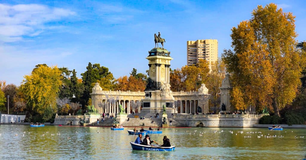 lake with people in rowboats in front of a colonnade with equestrian monument in the center; in Madrid Retiro Park 