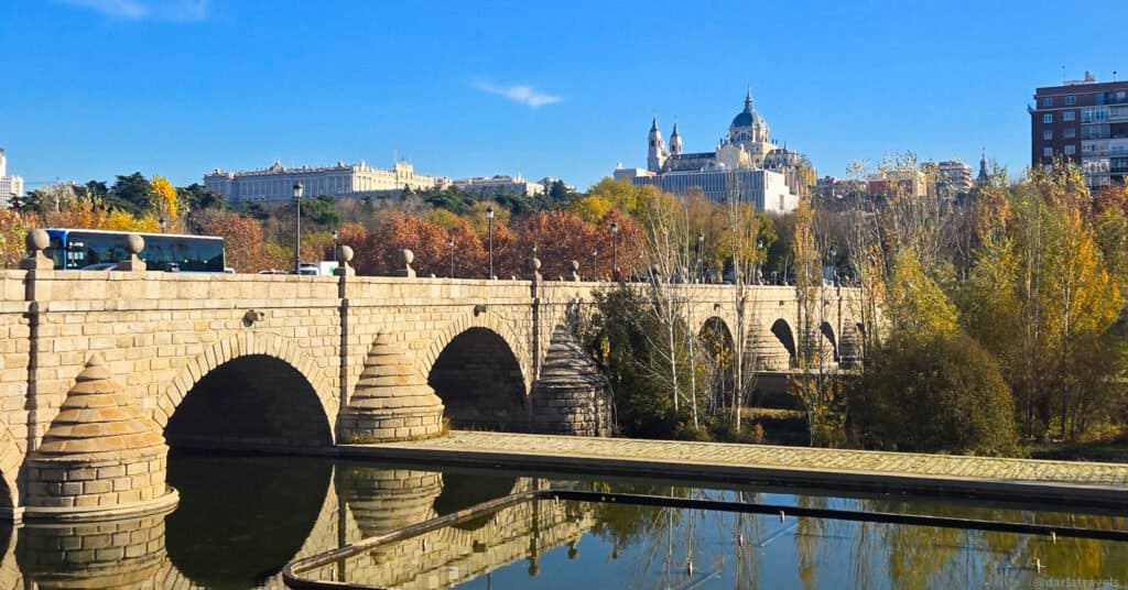 1800s era bridge crossing a river, hill with cathedral in the distance