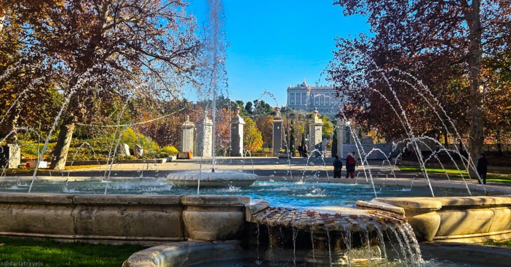 fountain with center water jet, water cascading over shell shaped basin, semicircle of pillars in the background