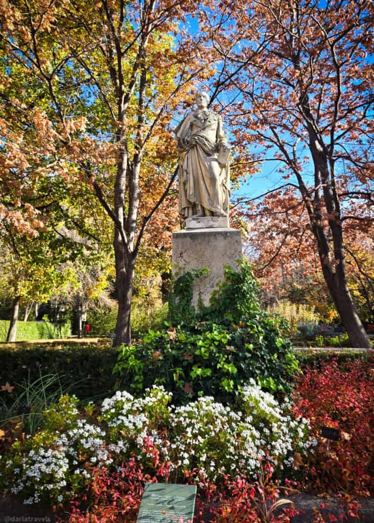 white statue of a man on a pedestal surrounded by flowering plants; Madrid Royal Botanical Garden