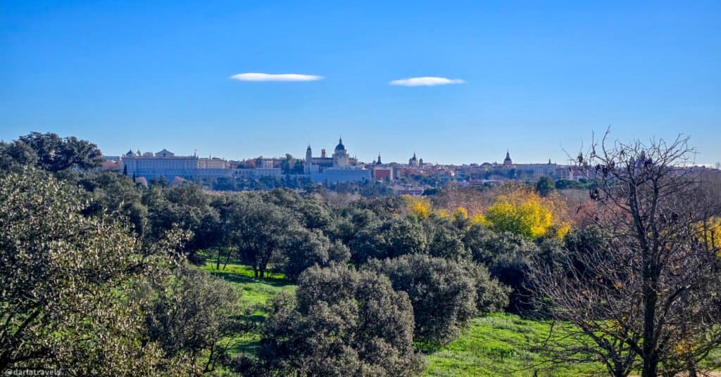 view over a grassy and bush-filled park to a city in the distance; Madrid,  Campo de Casa Park