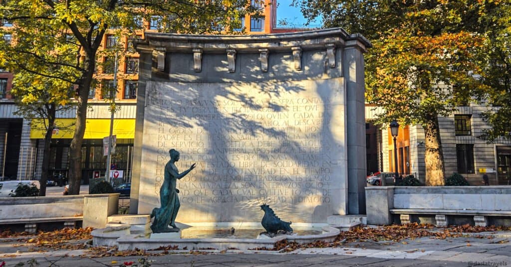 monument of curved wall with lettering. In front, bronze statues of a woman with an outstretched arm and four-legged creature