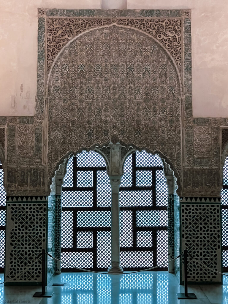 A photo of a doorway with an arched top and detailed plasterwork surrounding it. Below the arch is a lattice window with a geometric pattern.
