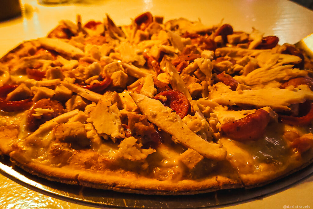 A freshly baked pizza topped with shredded chicken, pepperoni, and melted cheese, served on a thin, crispy crust. Perfect for pizza lovers looking for where to eat in Santa Marta, this dish offers a delicious combination of flavors at one of the city's top dining spots.