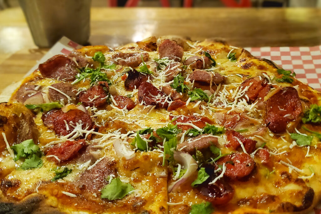 A freshly baked pizza loaded with salami, chorizo, onions, and melted cheese on a crispy, golden crust. If you're wondering where to eat in Santa Marta, this flavorful pizza is a top choice for food lovers exploring the city's best dining spots.