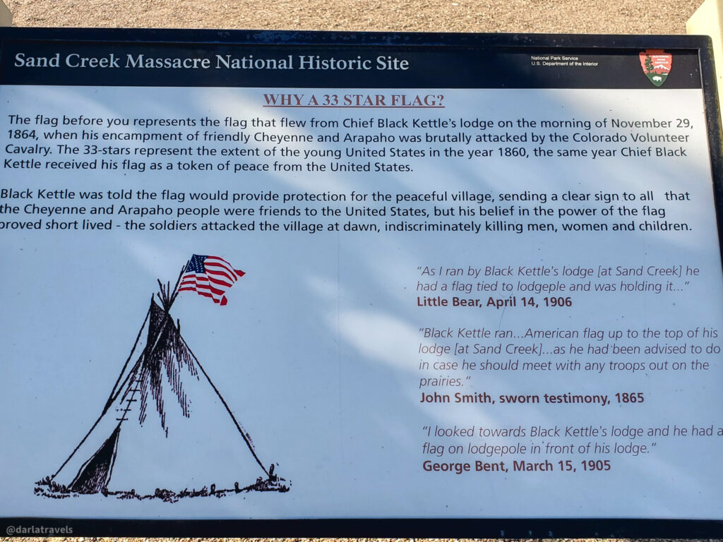 A rectangular sign titled "Sand Creek Massacre National Historic Site" provides information about a 33-star flag. The sign explains that the flag represents the one flown from Chief Black Kettle's lodge on the morning of November 29, 1864, when his encampment of friendly Cheyenne and Arapaho 1 people was attacked by the Colorado Volunteer Cavalry. It notes that the 33 stars symbolized the extent of the United States in 1860, and Chief Black Kettle received the flag as a token of peace from the United States. The sign features the National Park Service logo in the upper right corner.