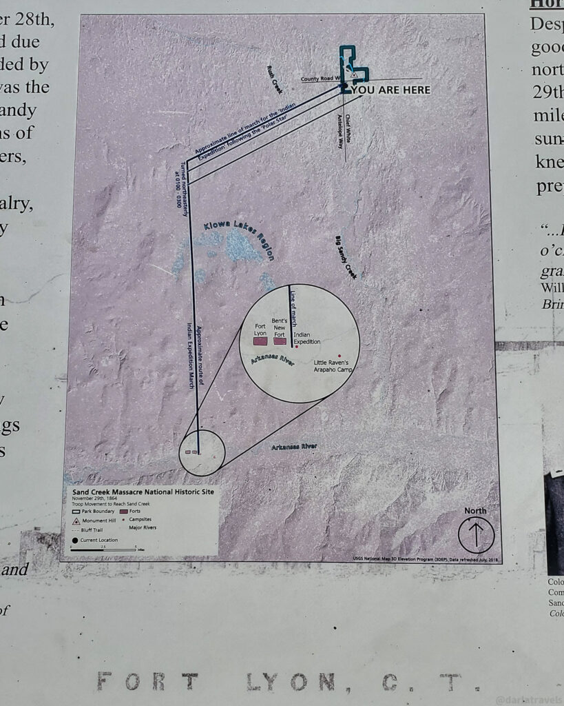 A portion of an informational sign at the Sand Creek Massacre National Historic Site displays a map titled "Sand Creek Massacre National Historic Site." The map shows the surrounding area with various landmarks and trails indicated. A blue square with the words "YOU ARE HERE" marks a specific location near Chief White Antelope Way and County Road W.
The map illustrates the approximate route of the "Indian Expedition March" towards Sand Creek, depicted by a thin line with arrowheads. It also shows Bent's New Fort, labeled in a circle encompassing the Indian Expedition route and Little Raven's Arapaho Camp near the Arkansas River. Kiowa and Lake Region are also marked on the map.
A legend in the lower left corner explains the symbols used, including markers for the Monument Hill. A compass rose indicating North is situated in the lower right corner of the map. The map provides a geographical context for the Sand Creek Massacre site.