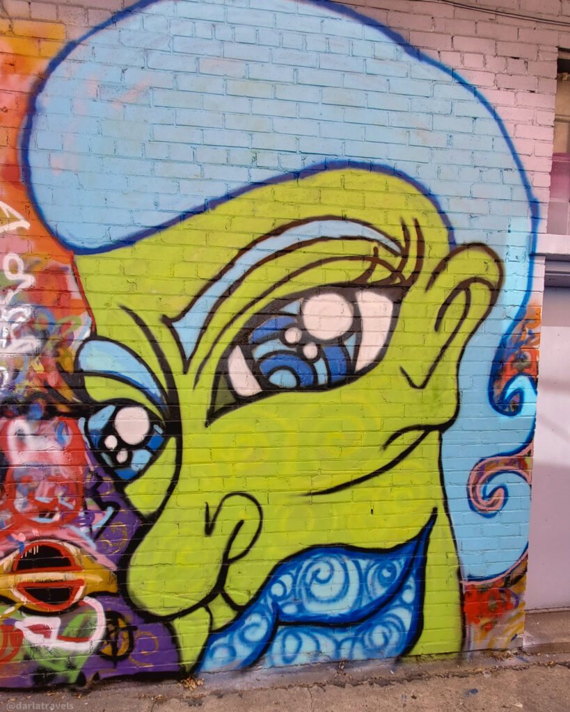 Bold graffiti face mural with green skin and blue hair in downtown La Junta, Colorado.
