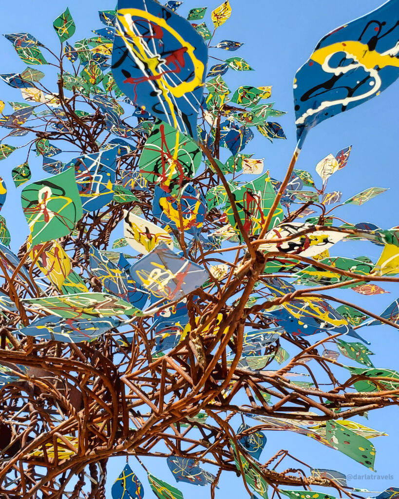 Colorful metal sculpture tree against blue sky in La Junta, Colorado public art display.