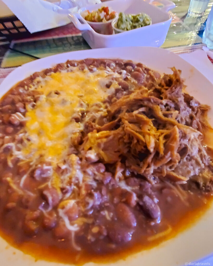 Hearty plate of beans, cheese, and shredded meat with guacamole and chips in La Junta, Colorado restaurant.