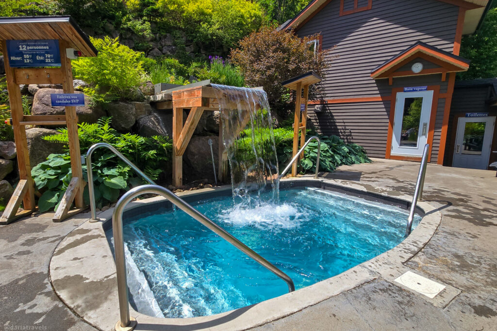 Outdoor cold plunge pool with waterfall feature, stone landscaping, and wooden signage near steam bath facility.