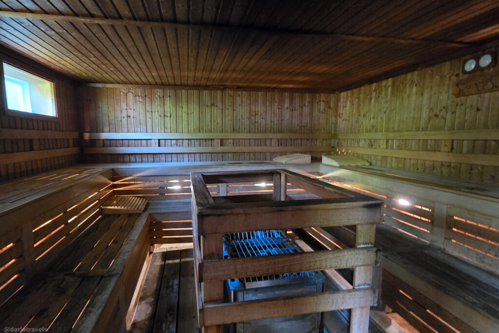 Wood-paneled sauna interior with a central stone heater, wooden benches, and soft natural lighting.