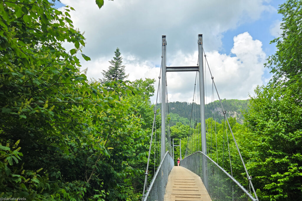 Suspension bridge with wooden walkway on Bras-du-Nord trail in Vallée Bras-du-Nord, surrounded by forest.