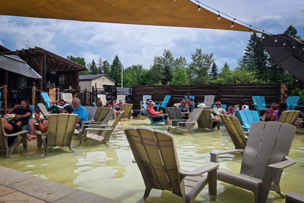 Outdoor seating in shallow water at Roquemount Brewery in Saint-Raymond, Quebec, shaded by canopy with string lights.
