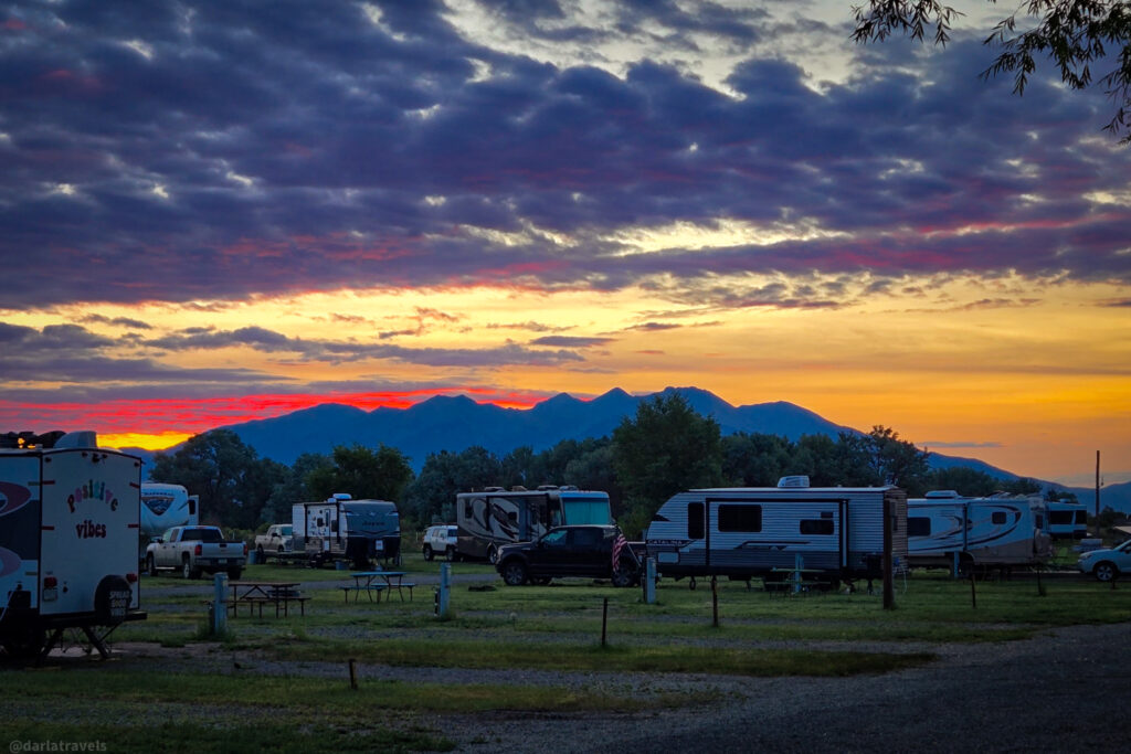 Campground with RVs, picnic tables, and sunset over mountain range in Alamosa, Colorado