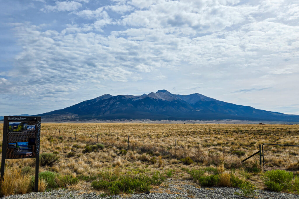 Dry grassy field with mountains in background and informational sign near Zapata Falls area in the San Luis Valley, Colorado