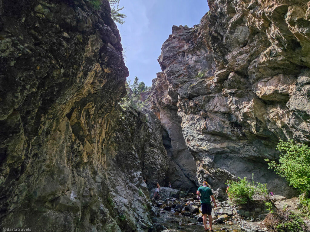 Hikers walking through narrow rocky canyon with stream and steep cliffs near Zapata Falls, Colorado