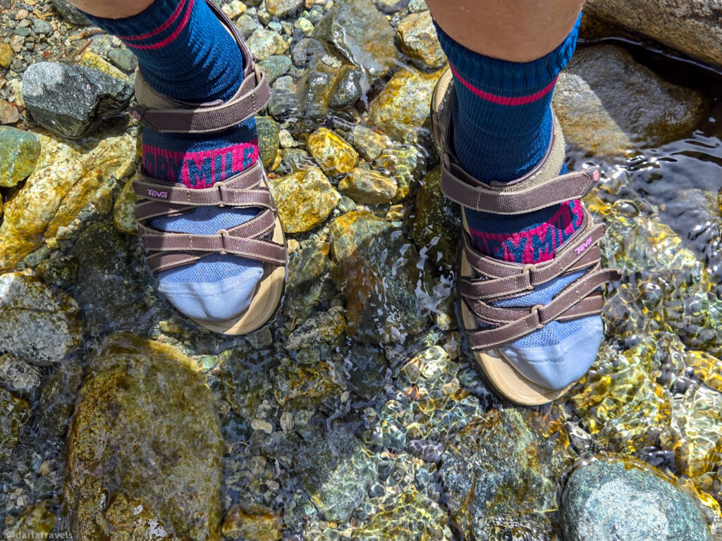 Feet in Teva sandals and âDRYMILEâ socks standing in shallow rocky stream near Zapata Falls, Colorado