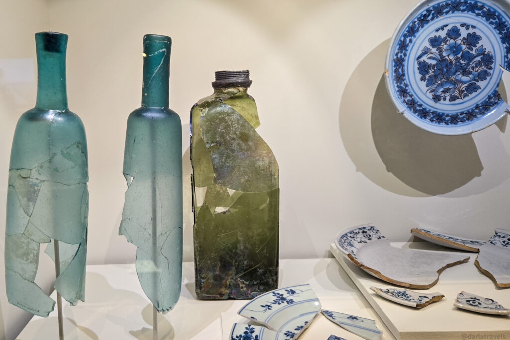 Historic glass bottles and blue-and-white ceramic fragments displayed in Quebec City archaeological exhibit
