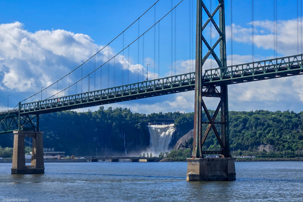 Orleans Island Bridge (Pont de l'Île-d'Orléans), suspension bridge spanning Saint Lawrence River with waterfall (Chute Montmorency) and forested cliffs in the background near Quebec City
