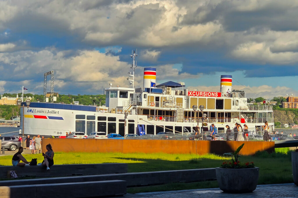 Excursion boat AML Louis Jolliet docked near Quebec City waterfront with striped smokestacks and park visitors nearby