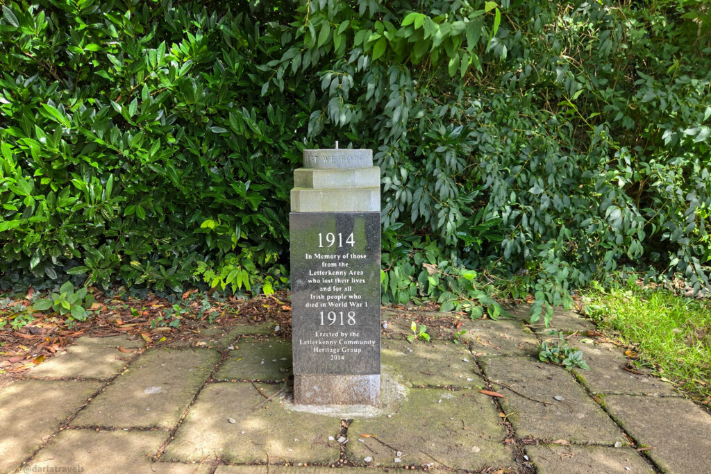 A World War I memorial stone, inscribed with dedication text, is set among lush green foliage and paving stones. Letterkenny, County Donegal Ireland