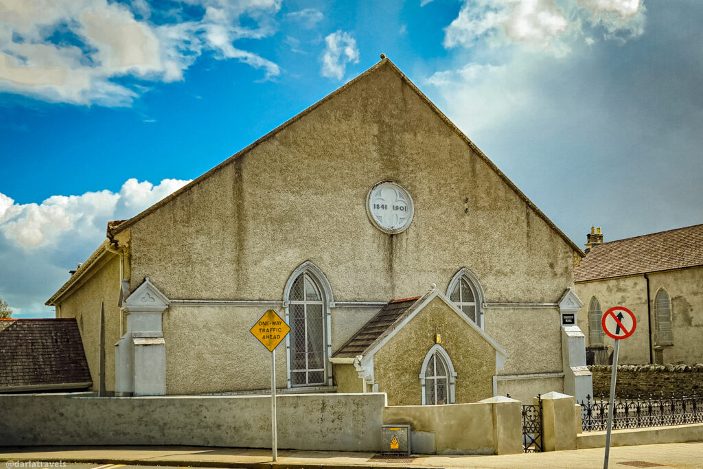 Historic church with textured beige walls, arched windows, a round plaque for 1841 and 1901, and street signs in foreground.