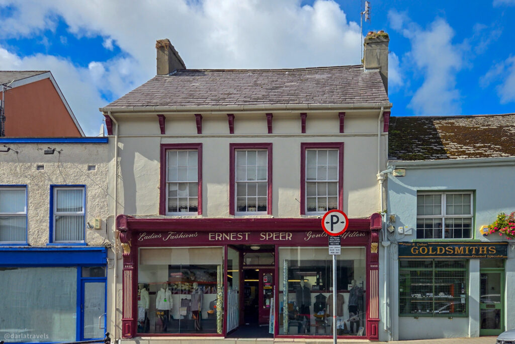 Traditional shopfront with mannequins in the window and a maroon sign reading “ERNEST SPEER” on a lively street.