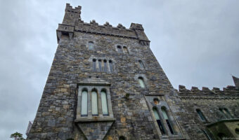 Glenveagh Castle tower with arched windows and crenellations under dramatic overcast sky in Donegal