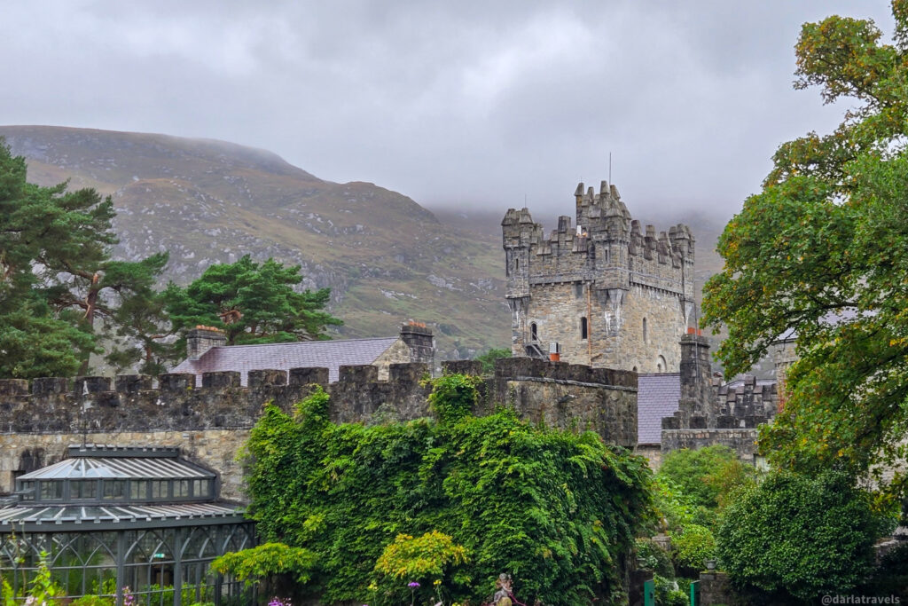Stone castle nestled in lush greenery with misty mountain backdrop; Glenveagh Castle in Donegal