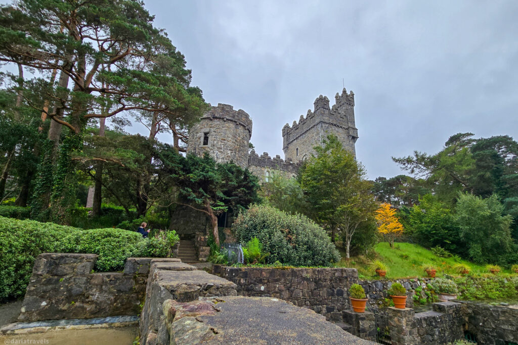 Round turret and crenellated tower of Glenveagh Castle framed by trees and terracotta pots in Donegal
