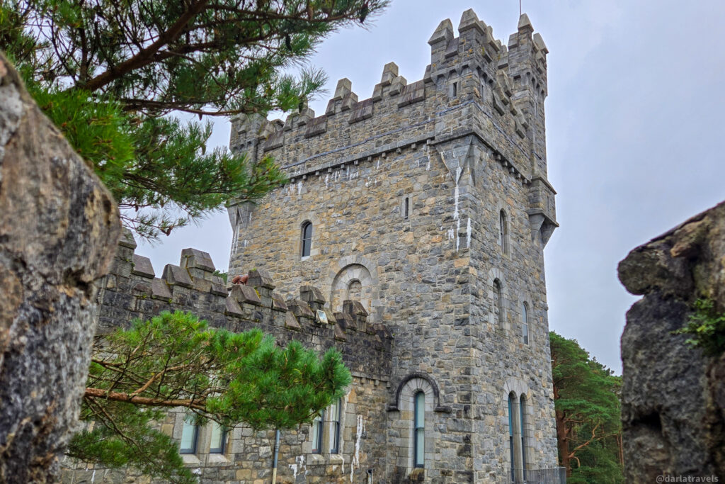 Castle tower with battlements and arched windows partially framed by rocks and trees in Donegal