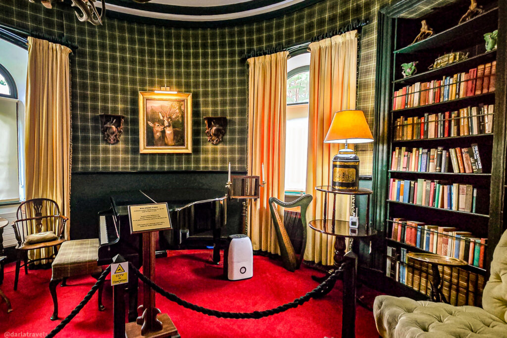 Circular red-carpeted room with mini grand piano , Irish harp, and mounted deer heads in Glenveagh Castle