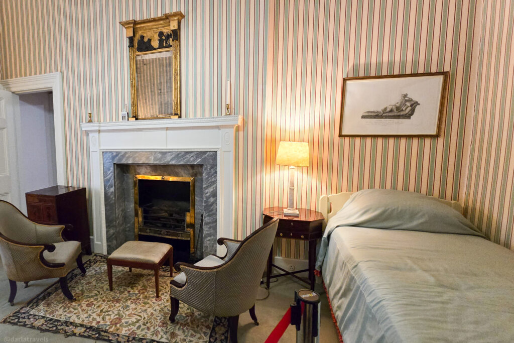 Single-bed bedroom with striped wallpaper, fireplace, and armchairs in Glenveagh Castle exhibit
