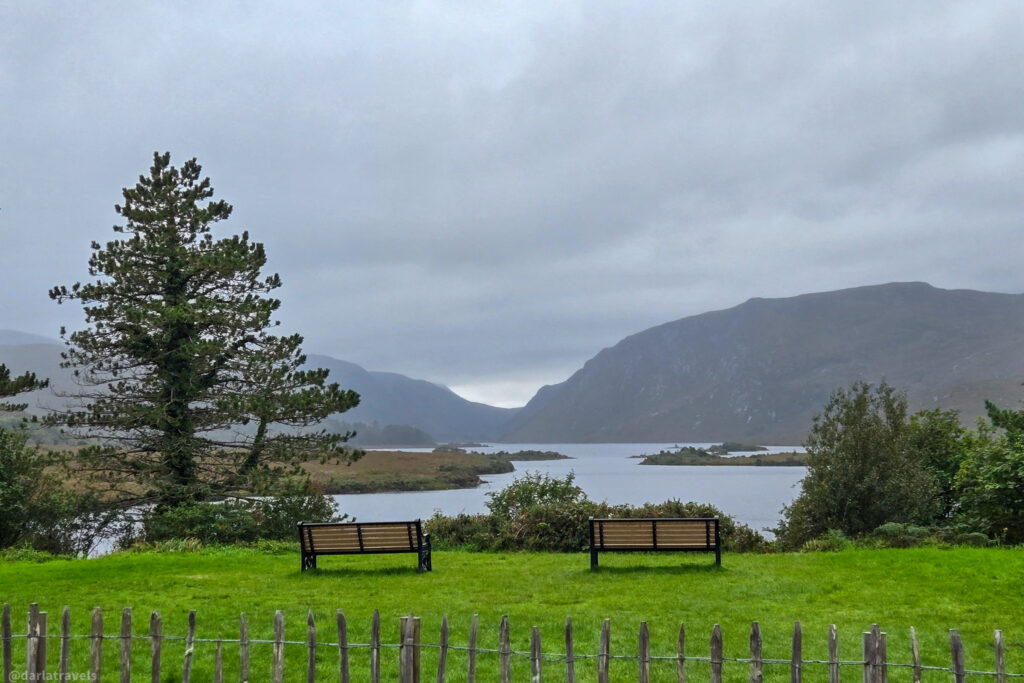 Benches overlooking lake and mountains near Glenveagh Castle, framed by pine tree and wooden fence