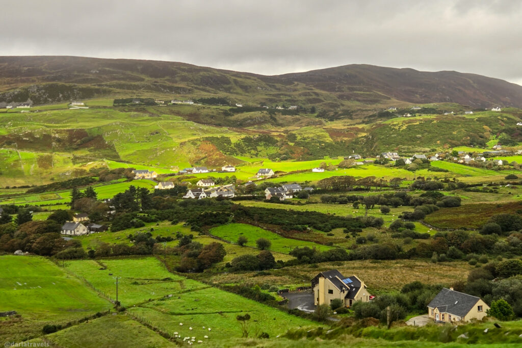 Rolling green Irish hills dotted with scattered white houses under a dramatic grey sky in County Donegal.