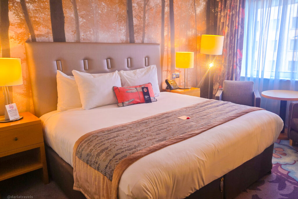 Cozy Dublin Airport hotel room with forest mural, padded headboard, and floral curtains
