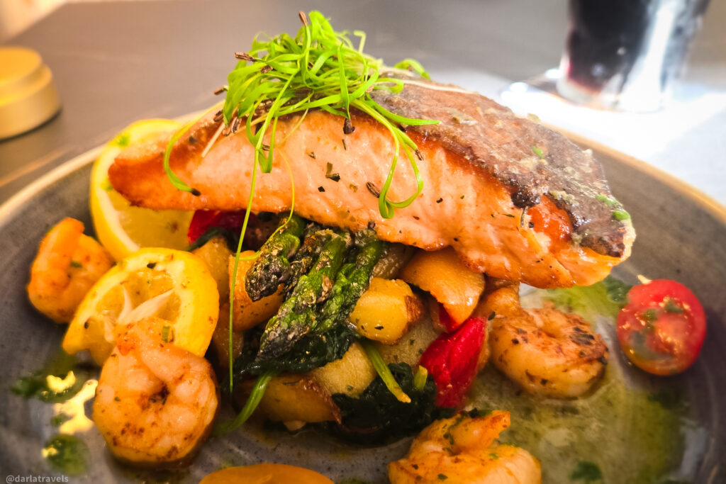 Seared salmon with shrimp, roasted vegetables, and microgreens