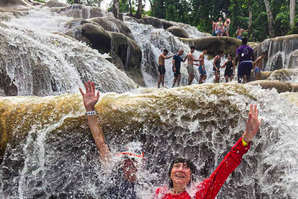 Climbers forming a line to ascend Dunn’s River Falls as water flows over two climbers on lower rocks.