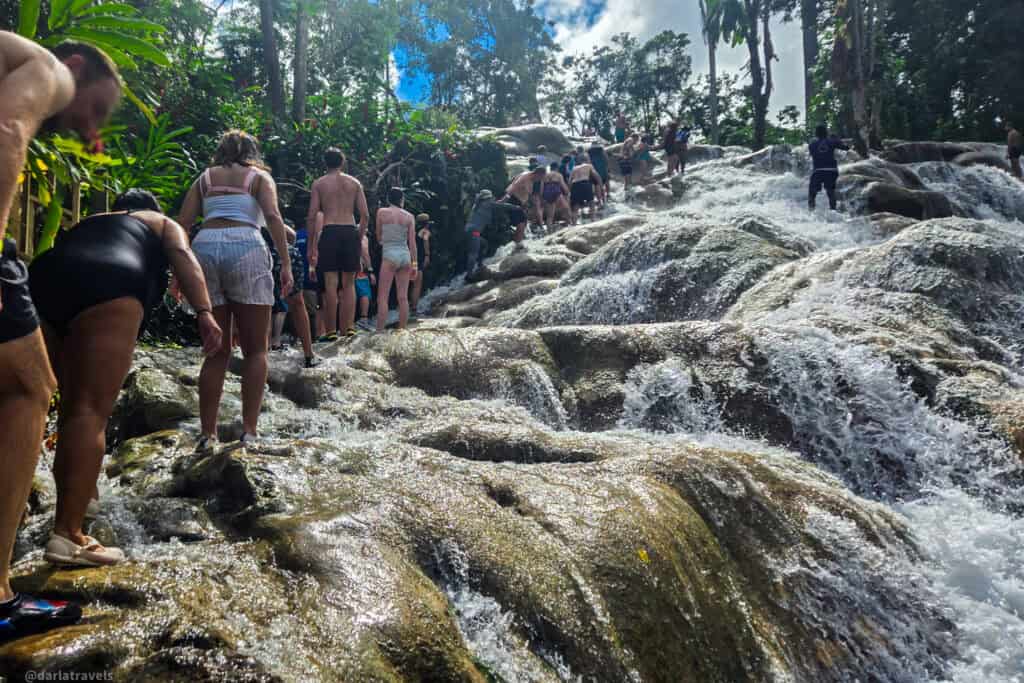 Climbers forming a line to ascend Dunn’s River Falls as water flows over the rocks.